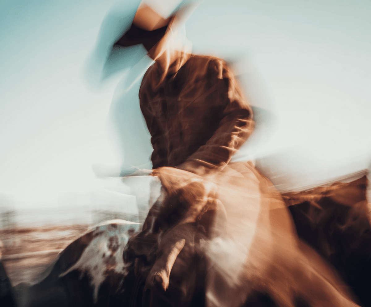 Motion-blurred rider in a brown duster and cowboy hat against a pale sky, the figure dissolving into speed