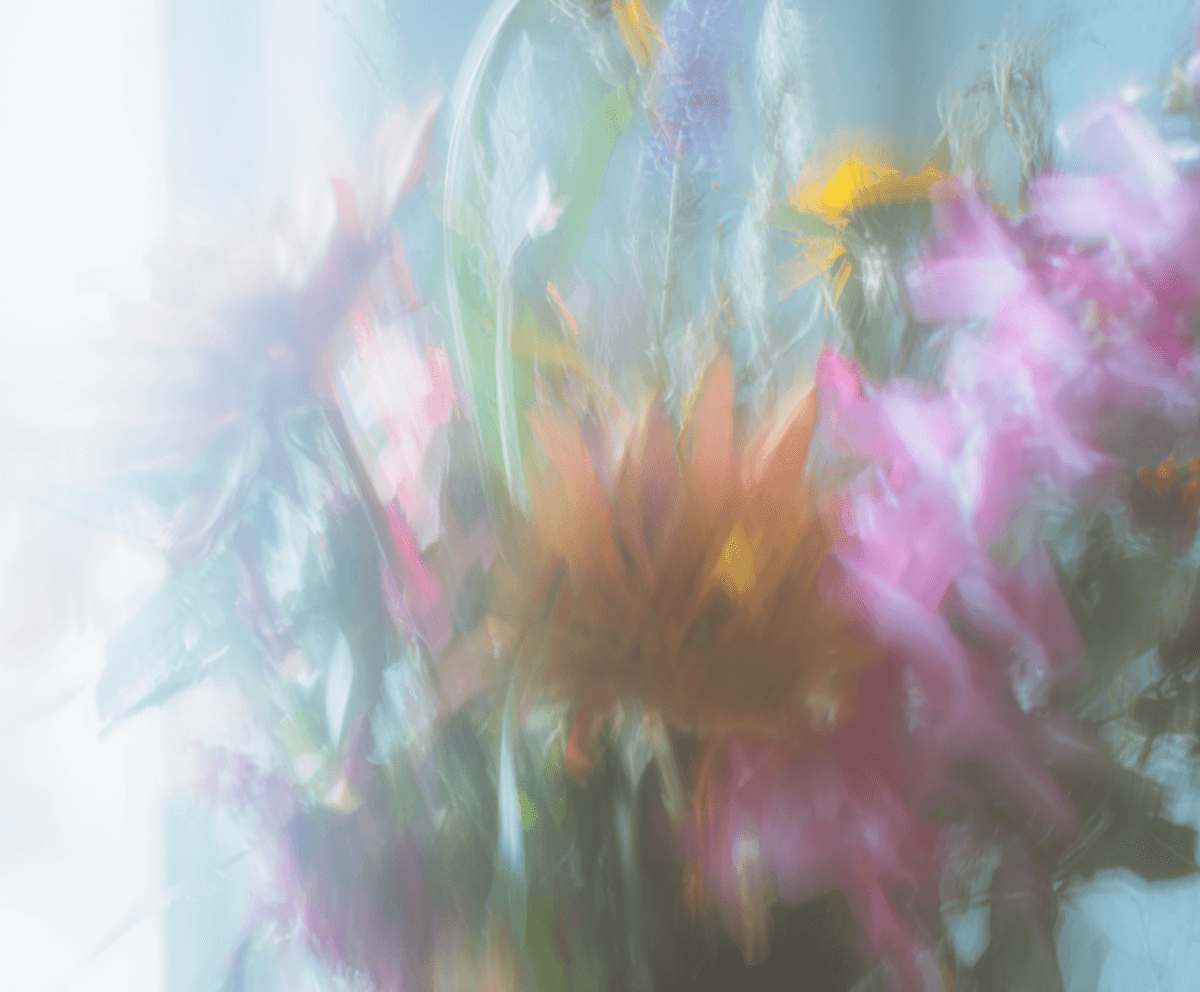 A blurred bouquet of pink, yellow, and lavender flowers behind soft glass, dissolving into pastel light
