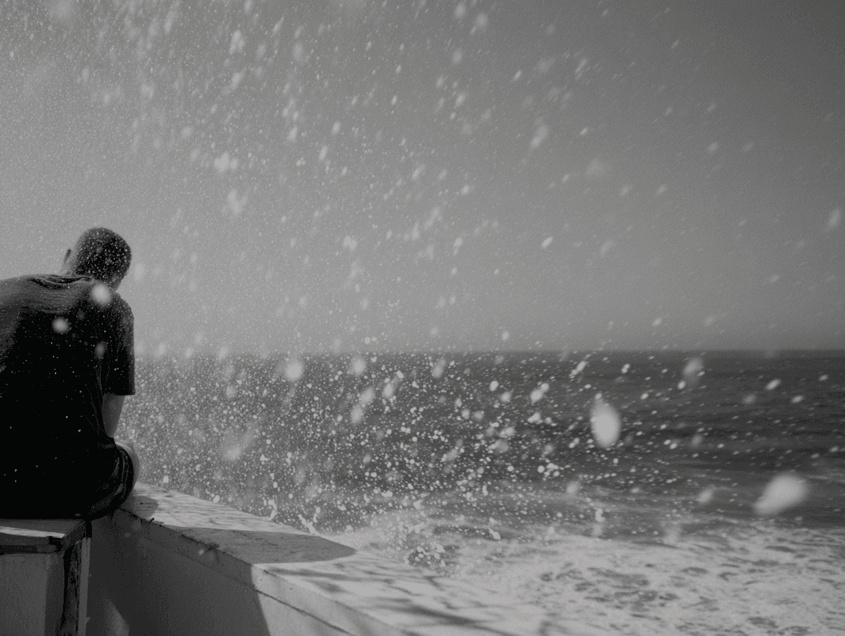 Black-and-white photograph of a lone figure on the bow of a small boat in heavy seawater spray